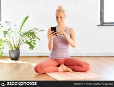fitness, technology and healthy lifestyle concept - happy smiling young woman with smartphone at home or yoga studio. woman with smartphone at home or yoga studio