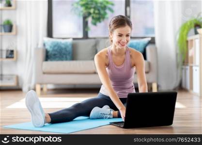 fitness, technology and healthy lifestyle concept - woman with laptop computer doing sports at home. woman with laptop computer doing sports at home