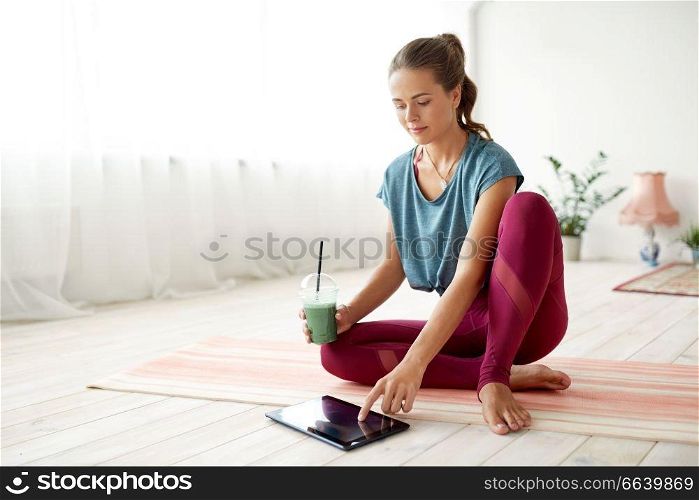 fitness, technology and healthy lifestyle concept - woman with tablet pc computer and cup of smoothie at yoga studio. woman with tablet pc and drink at yoga studio