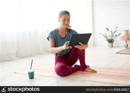 fitness, technology and healthy lifestyle concept - woman with tablet pc computer and cup of smoothie at yoga studio. woman with tablet pc and drink at yoga studio