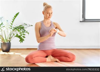 fitness, technology and healthy lifestyle concept - young woman with smart watch at home or yoga studio. woman with smart watch at home or yoga studio