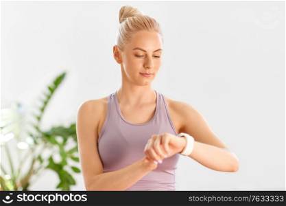 fitness, technology and healthy lifestyle concept - young woman with smart watch at home or yoga studio. woman with smart watch at home or yoga studio