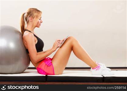 Fitness woman blonde fit girl sitting on floor and looking into tablet pc