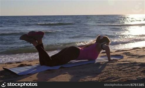 Fitness woman doing push-ups during sports training on beach at sunset