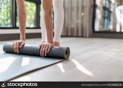 Fitness woman folding exercise mat before working out in yoga studio. rolling Yoga mat  after  training healthy lifestyle