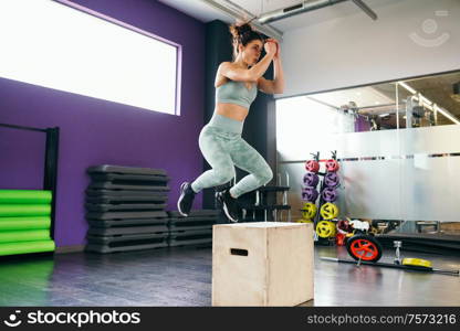 Fitness woman jumping onto a box as part of exercise routine. Caucasian female doing box jump workout at gym.. Fitness woman jumping onto a box as part of exercise routine.