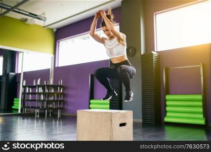 Fitness woman jumping onto a box as part of exercise routine. Caucasian female doing box jump workout at gym.. Fitness woman jumping onto a box as part of exercise routine.