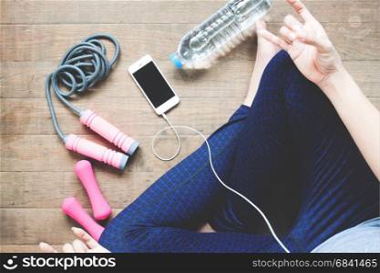 Fitness woman listening music on mobile device, Sport equipment, Bottle water on wood floor
