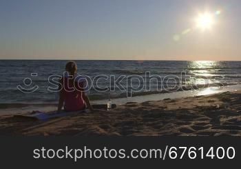 Fitness woman relaxing after workout routine listening music on beach at sunset rear view