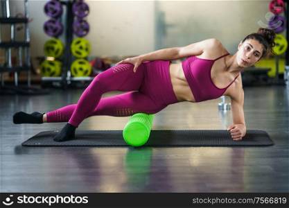 Fitness woman relaxing her leg muscles with a green foam roller at the gym. Woman relaxing her leg muscles with a green foam roller