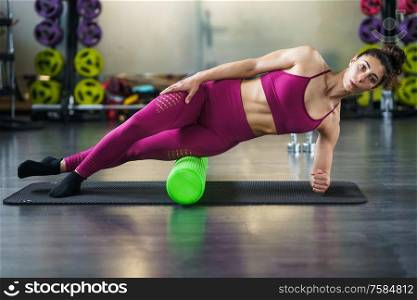 Fitness woman relaxing her leg muscles with a green foam roller at the gym. Woman relaxing her leg muscles with a green foam roller