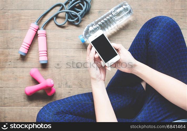 Fitness woman using mobile device, Sport equipment, Bottle water on wood floor