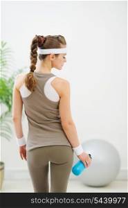 Fitness woman with bottle of water standing back to camera