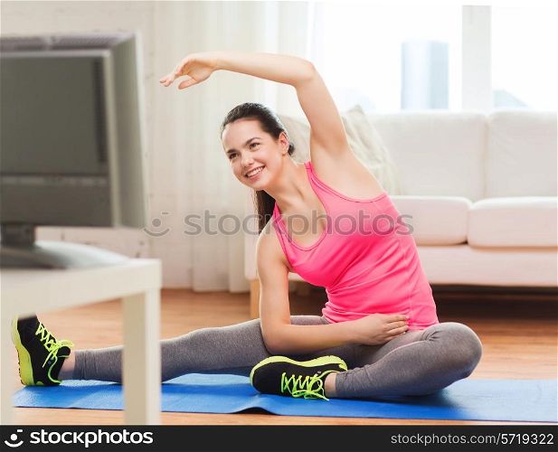 fitness, workout, healthy living and diet concept - smiling teenage girl stretching on floor and watching tv at home