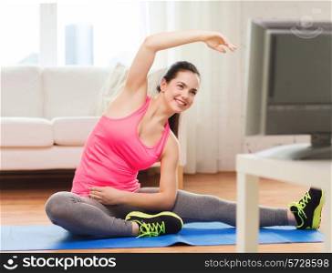 fitness, workout, healthy living and diet concept - smiling teenage girl stretching on floor and watching tv at home