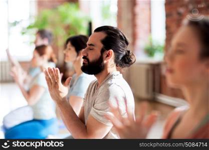 fitness, yoga and healthy lifestyle concept - group of people doing lotus seal gesture and meditating in seated pose at studio. group of people meditating at yoga studio. group of people meditating at yoga studio