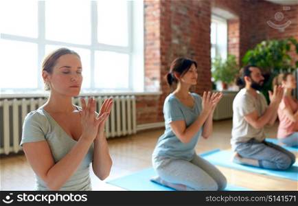 fitness, yoga and healthy lifestyle concept - group of people doing lotus seal gesture and meditating in seated pose at studio. group of people meditating at yoga studio