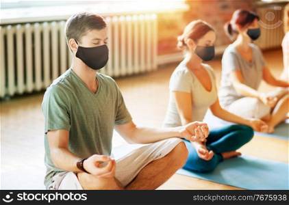 fitness, yoga and healthy lifestyle concept - group of people in black masks meditating at studio. group of people in masks doing yoga at studio