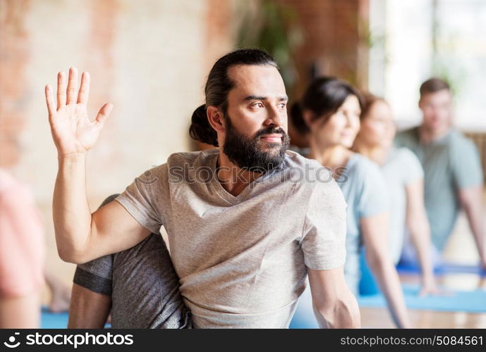 fitness, yoga and healthy lifestyle concept - man with group of people doing half lord of the fishes pose in gym or studio. man with group of people doing yoga at studio. man with group of people doing yoga at studio