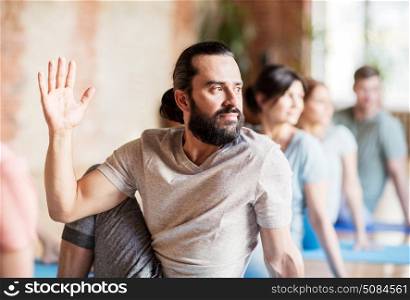 fitness, yoga and healthy lifestyle concept - man with group of people doing half lord of the fishes pose in gym or studio. man with group of people doing yoga at studio. man with group of people doing yoga at studio
