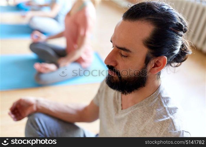 fitness, yoga and healthy lifestyle concept - man with group of people meditating in lotus pose at studio. man with group of people meditating at yoga studio