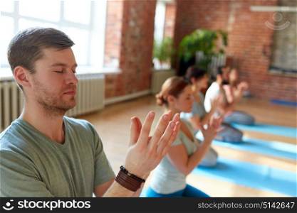 fitness, yoga and healthy lifestyle concept - man with group of people doing lotus seal gesture and meditating in seated pose at studio. man with group of people meditating at yoga studio