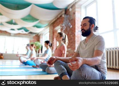 fitness, yoga and healthy lifestyle concept - man with group of people meditating in lotus pose at studio. man with group of people meditating at yoga studio