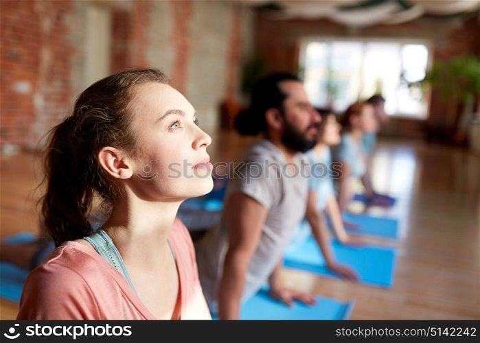 fitness, yoga and healthy lifestyle concept - woman with group of people doing cobra pose on mats at studio. group of people doing yoga cobra pose at studio
