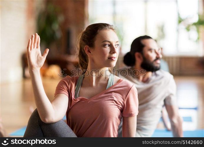 fitness, yoga and healthy lifestyle concept - woman with group of people doing half lord of the fishes pose in gym or studio. woman with group of people doing yoga at studio