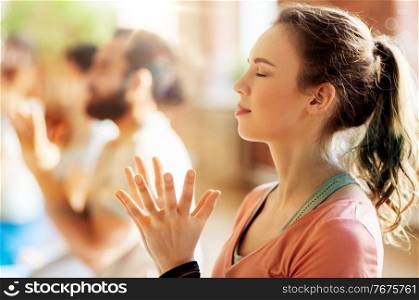 fitness, yoga and healthy lifestyle concept - woman with group of people doing lotus seal gesture and meditating in seated pose at studio. woman with group meditating at yoga studio