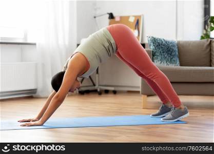 fitness, yoga and healthy lifestyle concept - young african american woman doing downward-facing dog pose at home. woman doing downward-facing dog yoga pose at home