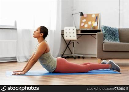 fitness, yoga and healthy lifestyle concept - young african american woman doing cobra pose at home. woman doing cobra yoga pose at home