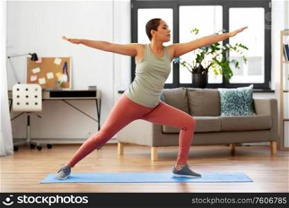 fitness, yoga and healthy lifestyle concept - young african american woman doing warrior pose at home. african woman doing yoga warrior pose at home