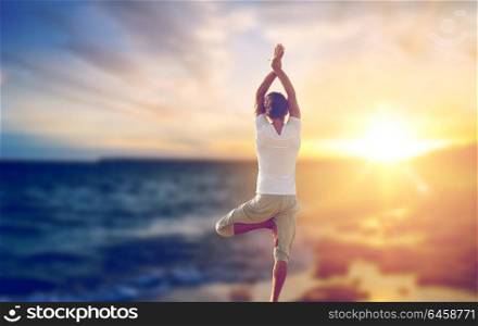 fitness, yoga and people concept - happy man making tree pose and meditating outdoors over sea background. happy man making yoga tree pose over sea