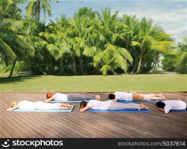 fitness, yoga and sport concept - group of people lying on mats over natural background with palm trees . group of people making yoga outdoors and lying