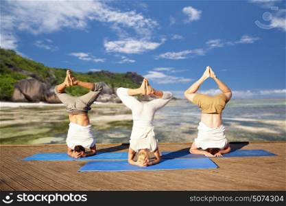 fitness, yoga and sport concept - people making headstand pose over exotic tropical beach background. people making yoga headstand on mat outdoors