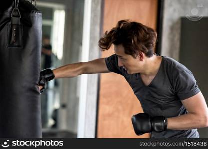 Fitness young American man training on punching bag with his right hand with gloves in sport gym. Muay Thai boxing training for bodybuilding and healthy lifestyle concept.