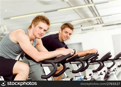 Fitness young man on gym bike spinning indoor cardio exercise