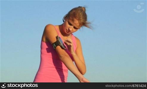 Fitness young woman touching phone screen in arm sport band before exercise outdoors