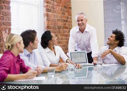 Five businesspeople in boardroom with laptop laughing
