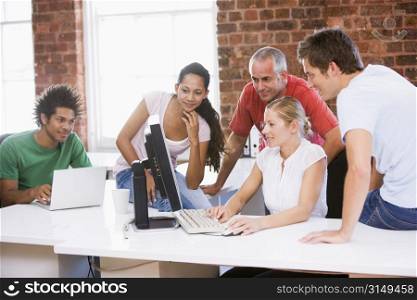 Five businesspeople in office space looking at computer and smiling