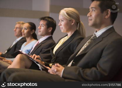 Five businesspeople sitting in presentation room with clipboards