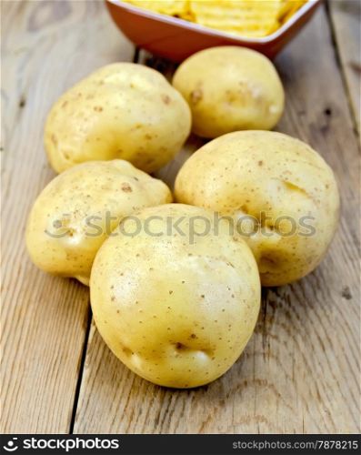 Five fresh yellow potato tuber, potato chips in a clay bowl on a wooden boards background