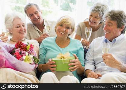 Five friends with champagne and gifts in living room smiling