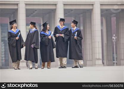 Five Graduate Students Standing and Talking With Diplomas