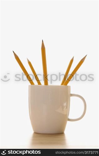 Five pencils in a coffee cup with pointed ends up.