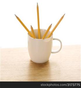 Five pencils in a coffee mug with pointed ends up.