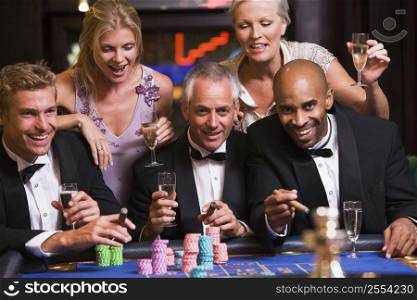 Five people in casino playing roulette and smiling (selective focus)