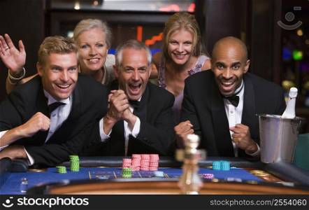 Five people in casino playing roulette smiling (selective focus)
