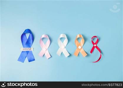 Five ribbons pink, white, blue, red, yellow, the word hope on sticky tape and pills lie in the center on a blue background, flat lay close-up. World cancer day concept.. Five multi-colored emblem ribbons on a blue background.